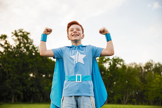 Young boy dressed as a superhero in blue costume standing outdoors confidently showing his strength.