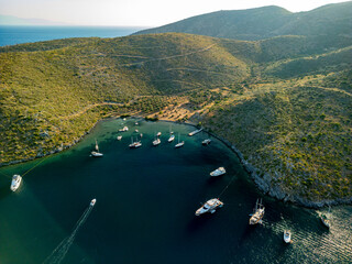Aerial view of boats dotting the tranquil, dark blue bay embraced by undulating green hills, a serene coastal panorama, Cokertme, Mugla, TÃ¼rkiye.