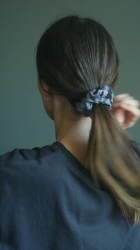 Long haired woman gathers her hair and creates a ponytail using a scrunchie, demonstrating the process step by step against a neutral background. Woman making a ponytail with scrunchie