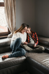 Mother and son relaxing with gadget on leather couch. Parents playing at tablet, engaged in screens activities. Family moment with teenager. Generation connection, indoor activity, technology