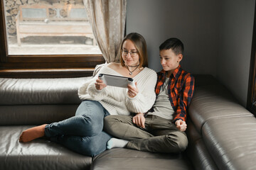 Woman and boy playing computer games. Teenager shares interest with parent on the tablet, on-line security. Parent control 