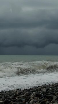 The stormy sky over the rocky seashore is a dramatic stormy landscape with heavy clouds in sea in overcast weather on pubble beach.. Waves washing stones on coastline. Slow motion cinematic shot.
