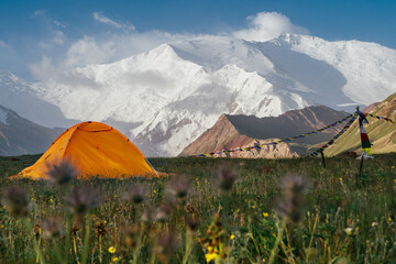 Bright yellow tent stands alone on green grass at 3600m Base Camp with vast panoramic view of Pamir...