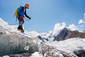 Climber in vibrant gear leaps over crevasse on icy glacier during Lenin peak ascent under clear sky...