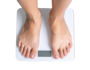 A person stands on a digital weighing scale, showing bare feet and a clear display for weight measurement.