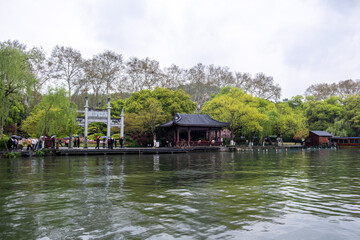 Hangzhou, West Lake. China. Tourists with umbrellas walk along the promenade by a traditional Chinese pavilion