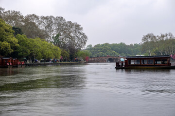 Hangzhou, West Lake. China. Tourists walk along the Lake promenade, traditional stone bridge and wooden boat