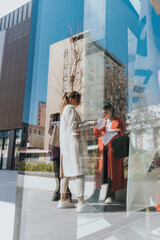 A group of three women stand outdoors, discussing documents while surrounded by modern buildings....