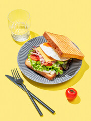 Club sandwich with egg, bacon, cheese, tomatoes, lettuce and sauce in a plate on a yellow background