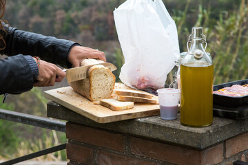 A person cuts bread on a cutting board beside a bottle of olive oil
