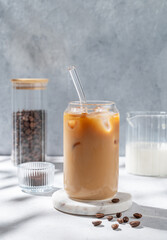 Ice latte coffee in a glass with milk on a marble stand on a light background with coffee beans