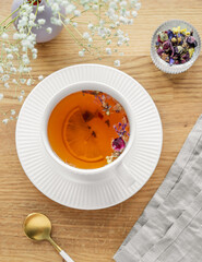 A cup of herbal tea with lemon and bouquet of flowers on a wooden table with napkin.