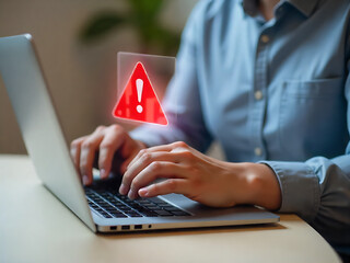 A person uses a laptop with a red warning icon on screen, suggesting a tech issue. The setting is softly lit with a blurred background.