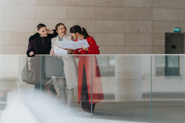 Three female entrepreneurs standing in a modern office space, collaboratively reviewing documents...