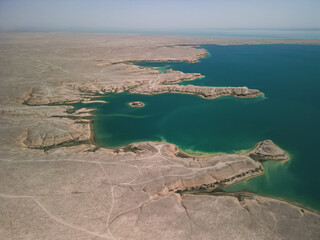 Peninsula and island surrounded by blue waters of Kuimazar Reservoir. The barren, dry landscape contrasts with the vivid color of the water in Uzbekistan