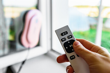 Woman's hand holding remote control of window cleaner robot.