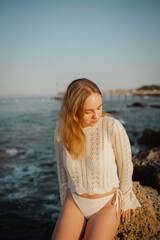 beautiful young girl with a beautiful athletic figure of European appearance in a swimsuit and underwear on the ocean shore in the open air. Sea waves and rocks with blue water. Travel and recreation