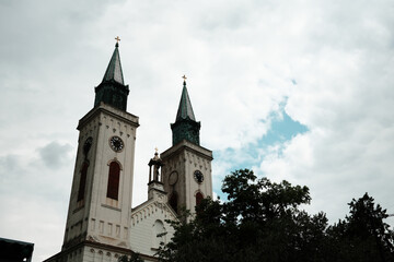 Fototapeta premium Close-up view of the twin clock towers of a Catholic church in Sombor, Serbia, showcasing architectural detail and statue above the entrance. Carmelite Church of Saint Stephen of Hungary