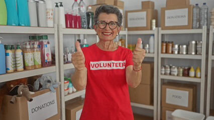 Senior woman with grey hair smiling and giving thumbs up while volunteering in a donation stockroom...