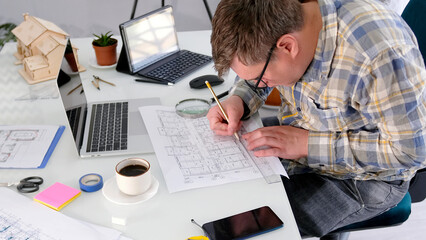 A design engineer at work. The architect is sitting at a table with a laptop, a cell phone, a...