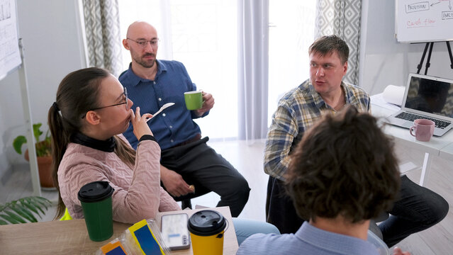 Coffee break. A group of people are sitting at a table with cups of coffee and a laptop. Business lunch. The company talks about general topics