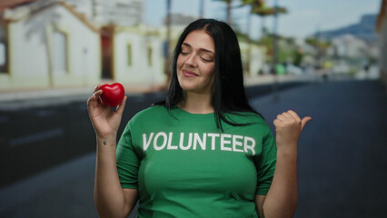 Curvy young woman volunteer confidently stands on a city street holding a red heart-shaped object...