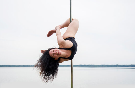 young woman in black swimsuit practicing poledancing on nature. Health conception.