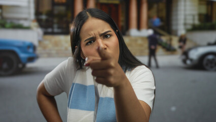 Woman extends finger while pointing down a street as young latin hispanic angry speaker looks into...