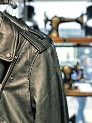 Leather Jacket Detail: A stylish black leather jacket, showcasing intricate details and textures, hangs elegantly against a soft-focus backdrop of a vintage sewing machine.