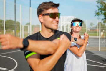 Dynamic duo stretches in a sunny sports complex for fitness