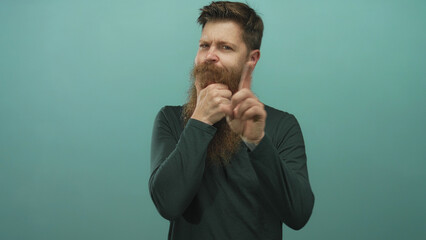 Man with beard and hand on chin in studio with mint green backdrop looking aside; contemplation.