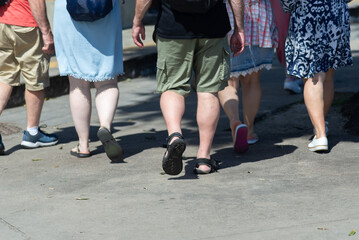 Half-body view of unidentified people walking down a street from a sidewalk. Pedestrians.