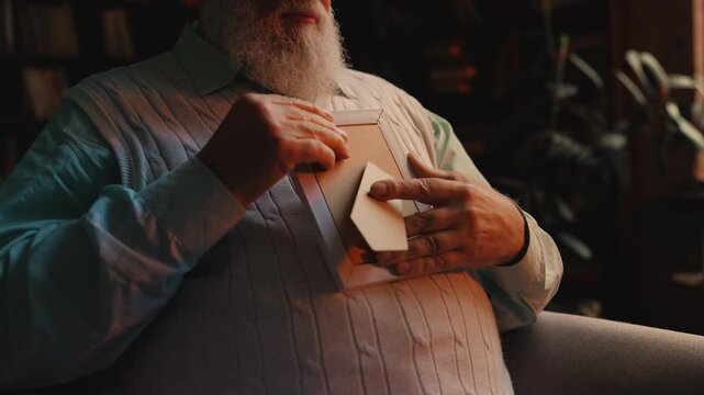 Upset senior man looking at family photo, missing loved ones, feeling loneliness
