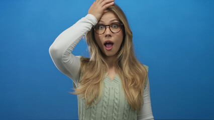Adult caucasian woman with long blonde hair wearing eyeglasses showing open mouth gesture in blue...