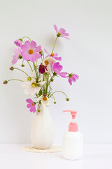 Summer still life with a bouquet of fresh delicate pink cosmos flowers and a bottle of natural...