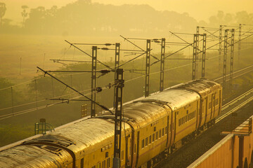 Indian Passenger Train at Sunrise with Misty Golden Light and Overhead Electric Wires