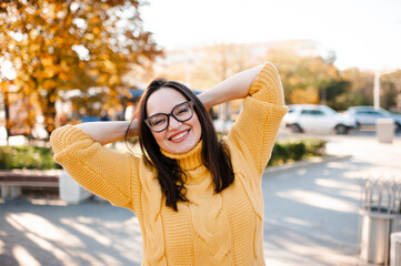 Smiling mature woman 35-40 year old wearing eye glasses and knitted yellow sweater over autumn city background close up. Fall season. Happiness.