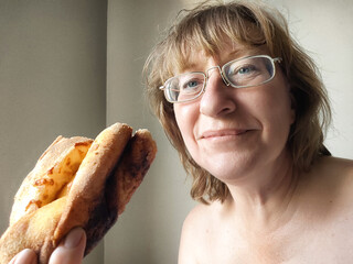 Middle-aged woman enjoys khachapuri after waking up in cozy bedroom setting, showcasing relaxed morning lifestyle