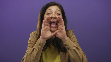 Middle aged hispanic woman shouting with cupped hands and open mouth in purple studio setting;...