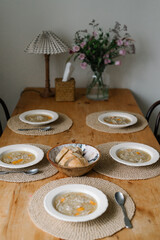Chicken noodle soups on the wooden vintage dining table, loaf of bread, aesthetic table setting...