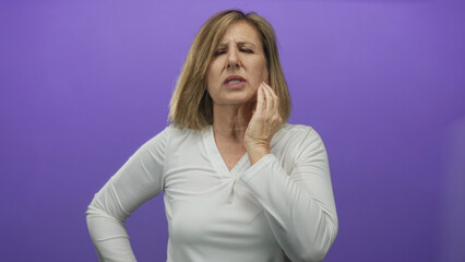 Middle age woman pressing cheek with hand and frowning in purple studio portrait; toothache...