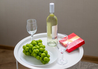 Bottle of white wine, large grapes, box of chocolates, wine glasses on the small coffee table. Celebration