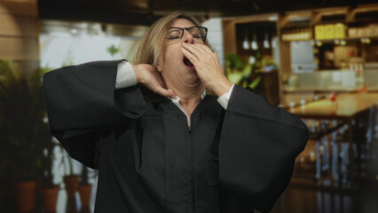 Woman in black robe stretching arms and yawning in a restaurant building interior; judicial fatigue.