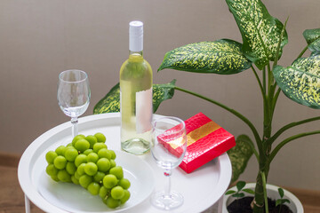 Bottle of white wine, large grapes, box of chocolates, wine glasses on the small coffee table. Celebration