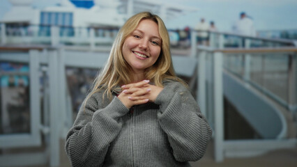 Young blonde woman smiling on cruise ship deck with casual attire, enjoying outdoor seaside view on...