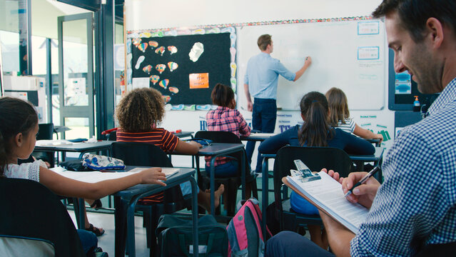 Male Trainee Teacher Being Observed Teaching In Classroom By Supervisor