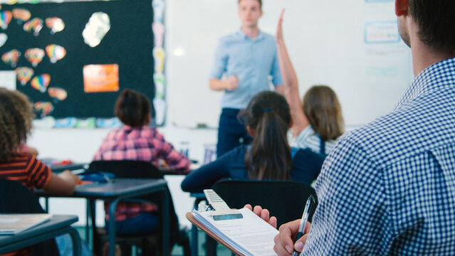 Male Trainee Teacher Being Observed Teaching In Classroom By Supervisor