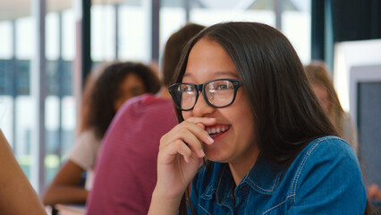 Smiling Female High School Student Wearing Glasses Sitting At Desk During Lesson