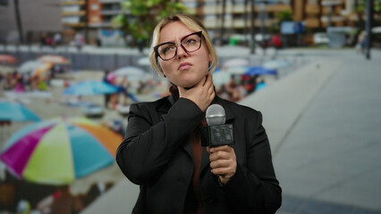 Woman reporter at seaside holding microphone while adjusting glasses and speaking against a vibrant...