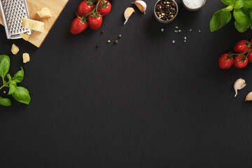 Fresh Italian ingredients like cherry tomatoes, garlic, basil, cheese, salt, and pepper on black...
